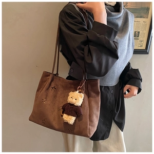 Détail du sac cabas en daim marron avec motifs floraux découpés au laser et breloque ours