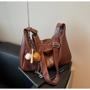 Close-up of caramel brown leather tote bag featuring a unique baseball theme pendant