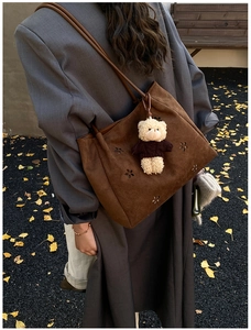 Détail du sac cabas en daim marron foncé avec découpes florales et charm d'ours mignon