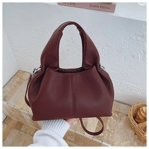 Vue détaillée d'un sac seau bordeaux à texture litchi sur des marches en pierre au soleil