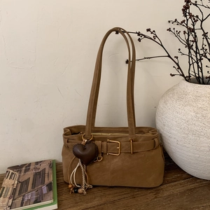 Detail of khaki leather shoulder bag with decorative belt buckle and heart charm on table