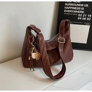 Detail of dark brown leather tote bag showing white contrast stitching and baseball charm