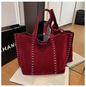 Détail d'un sac cabas en daim rouge avec rivets argentés et finitions de style industriel