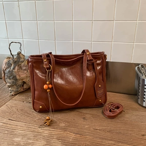 Detail of vintage brown leather tote bag with bead tassel charm and brand logo