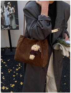 Détail d'un sac cabas marron avec découpes florales et un pendentif ours en peluche