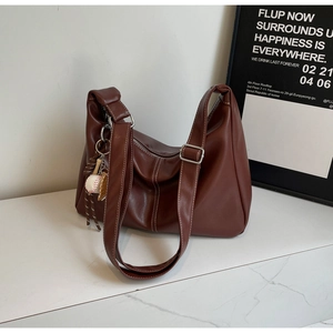 Detail of dark brown leather hobo bag with contrast stitching and baseball charm on bag