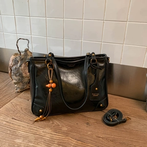 Detail of black vintage leather tote bag with metallic studs and pumpkin tassel charm