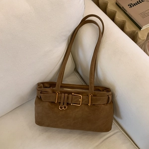 Close-up of vintage brown leather underarm bag with gold buckle on a white sofa