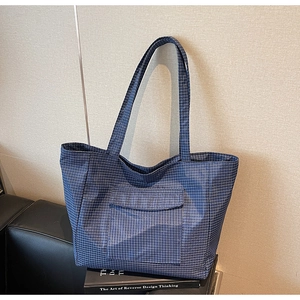Detail of blue plaid tote bag with front pocket on a black leather surface