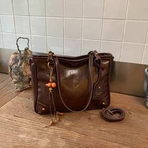 Detail of dark brown vintage tote bag with wooden charm and strap on wooden table