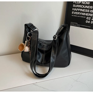 Detail of black tote bag with white contrast stitching and baseball charm on marble table