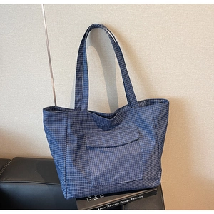 Detail view of navy blue checkered tote bag with front pocket on a leather sofa