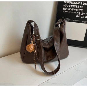 Detail of dark brown leather tote bag featuring contrast stitching and leaf charm