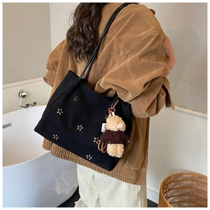 Détail du sac cabas en toile noire avec découpes florales et breloque ours en peluche