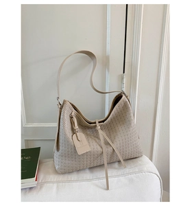 Détail du tissage et du pompon décoratif sur un grand sac à bandoulière beige chic