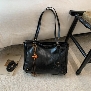Close-up of black leather tote with wooden bead tassel and luggage tag on white carpet