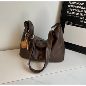 Detail of dark brown leather tote bag with white stitching and strawberry charm decoration