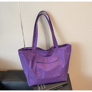 Detail of purple checkered tote bag featuring a front flap pocket on a leather surface