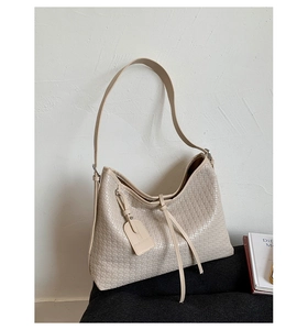 Gros plan d'un sac à bandoulière beige tissé avec pompon en cuir et étiquette amovible
