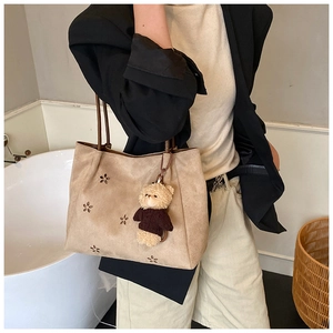 Détail du sac à main en daim kaki avec motifs de fleurs évidés et pendentif ours en peluche