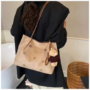 Detail view of large faux suede tote bag with laser-cut floral patterns and bear pendant