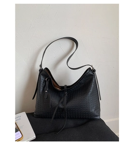 Détail de la texture tressée noire du grand sac hobo avec cordon à pompon élégant