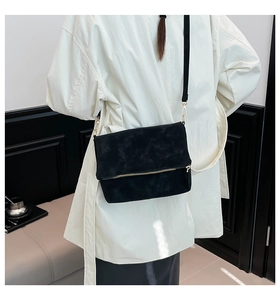 Detail of black suede crossbody bag with gold zipper and model carrying it on shoulder