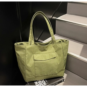 Detail of green checkered tote bag showing the front flap pocket and textured fabric
