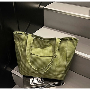 Detail shot of green checkered canvas tote bag with functional front pocket on urban steps