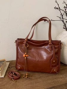 Retro brown leather tote bag with wood charm on wooden table in elegant setting