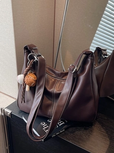 Brown hobo shoulder bag with contrast stitching and baseball pendant on a wooden surface