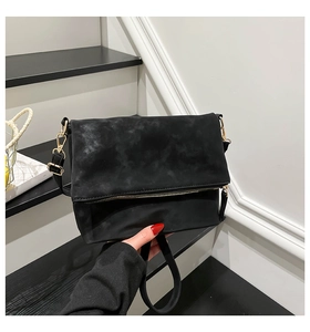 Detail of black suede shoulder bag featuring gold hardware and functional zipper accents