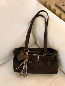 Retro dark brown matte leather handbag with golden buckle and heart tassel on a sofa