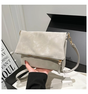 Detail view of a light gray folding crossbody bag featuring gold metal zipper and hardware