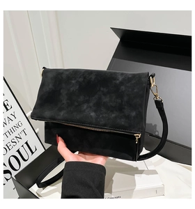 Detail of minimalist black suede crossbody bag featuring gold zipper and metal hardware