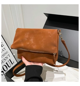 Detail of caramel suede fold-over crossbody bag with metal zipper and slim strap