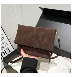 Close-up of dark brown suede crossbody bag showing metal zipper and foldable flap design