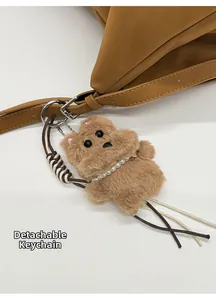 Detalle de un colgante de oso de peluche desmontable con collar en un bolso de cuero