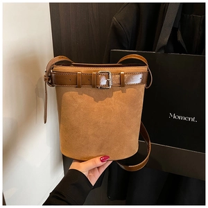 Close-up of brown suede bucket bag featuring leather belt buckle detail and slim strap