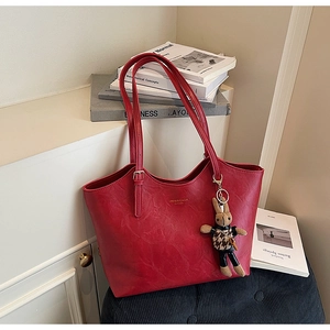 Detail of red lychee grain leather tote bag with gold logo and plush rabbit pendant