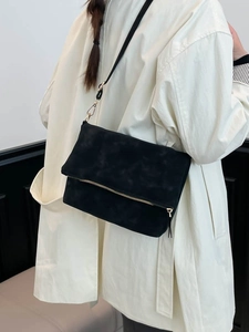Minimalist black faux suede shoulder bag with gold zipper detail and adjustable strap