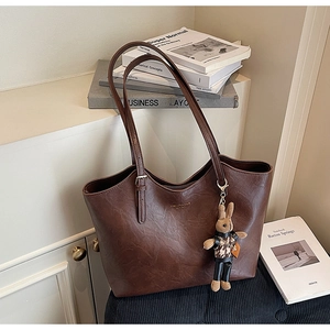 Detail of dark brown leather tote bag showing vintage texture and plush rabbit charm
