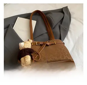 Close-up of vintage brown embossed underarm bag featuring a buckle strap and bear charm