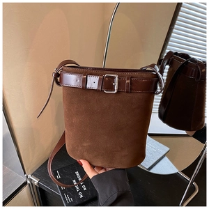 Close-up of a dark brown suede bucket bag featuring a belt buckle detail and leather strap