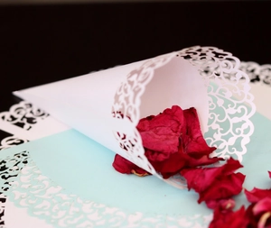 Close-up of white laser-cut confetti cone with elegant hollow pattern and red rose petals