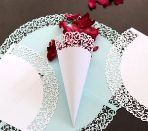 Close-up of laser-cut white lace wedding petal cone with intricate floral vine hollow details