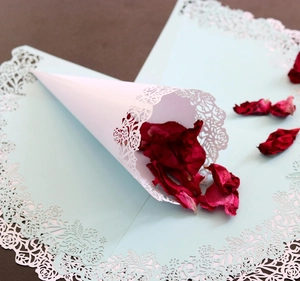 Detailed laser-cut rose lace pattern on white wedding confetti cone with flower petals