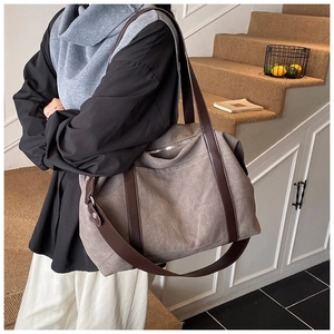 Detail view of large canvas tote bag with brown leather straps worn on shoulder