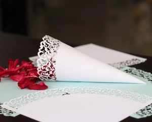 Detailed laser-cut white wedding paper cone with intricate lace vine pattern for petals