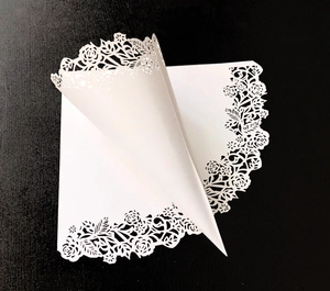Detail of laser-cut rose patterns on white wedding petal confetti cones made of cardstock